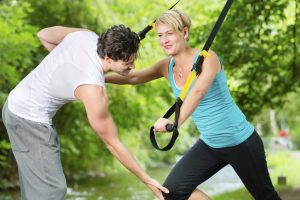 A woman pulling a cable pull with the guidance of a coach.