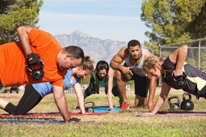 People planking with one hand lifting a kettlebell guided by a coach