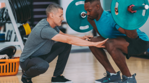 A black man lifting a dumbbell with a coach help