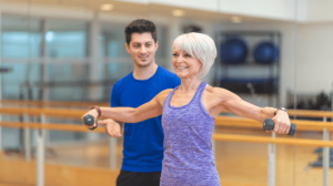 An old woman doing workout with a small barbell with a coach supervision