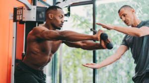 A man pulling exercise cables in the presence of a personal trainer