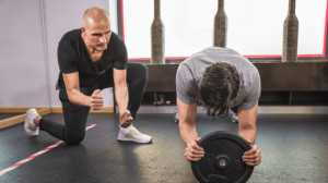 A personal trainer motivating and instructing a trainee on his planking